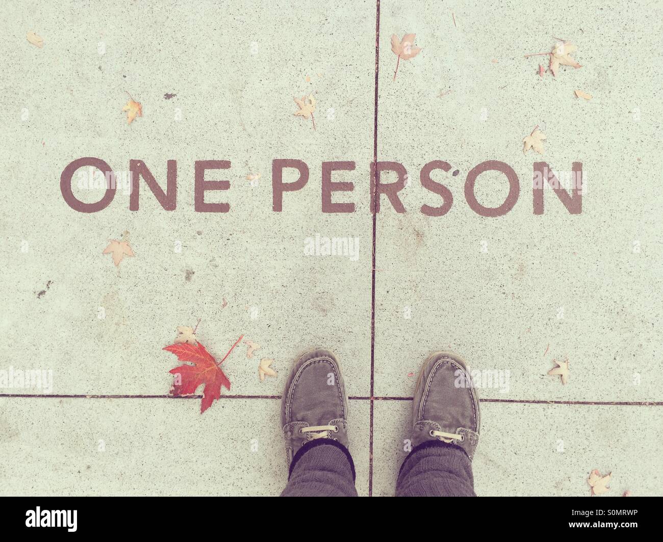 POV. Mirando hacia abajo en el texto que dice "una persona" en la acera, con una hoja de otoño cerca de mis pies. Foto de stock