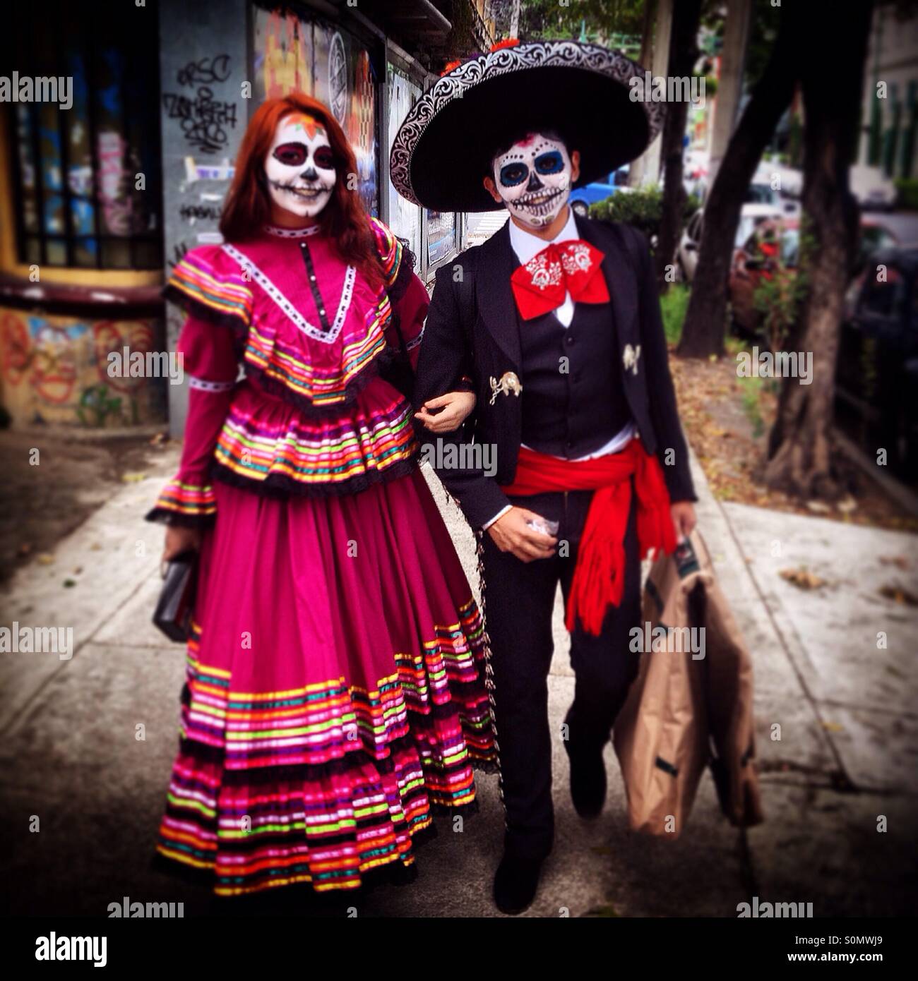 Un par de mexicanos vestidos con los trajes tradicionales de las  celebraciones del Día de los Muertos caminando por una calle de la Colonia  Roma, Ciudad de México, México Fotografía de stock -