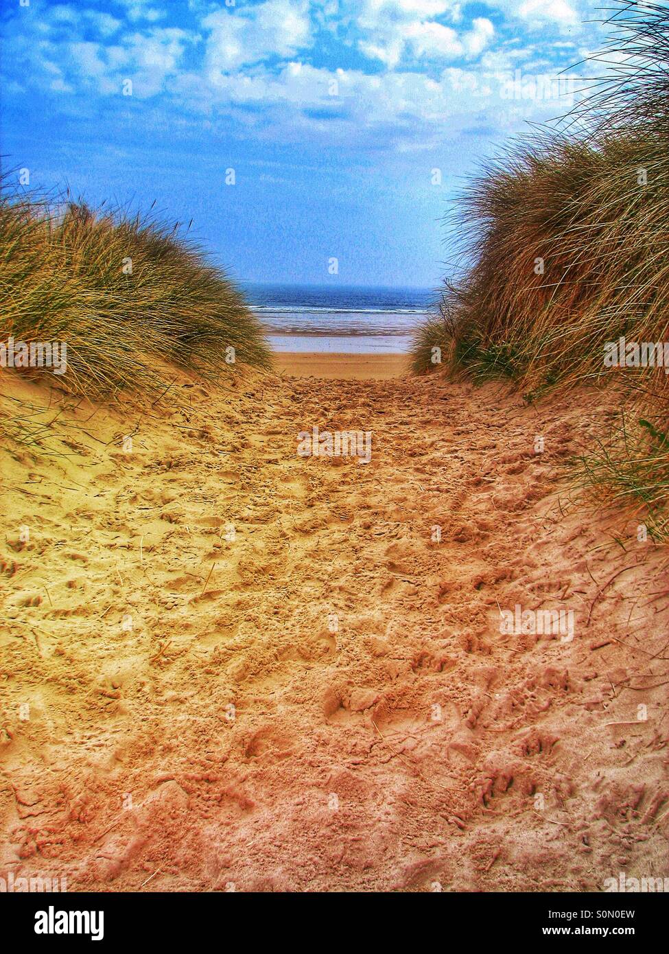 Un sendero de arena a través de las dunas de arena de una hermosa playa con vista al mar y cielo azul. Foto de stock