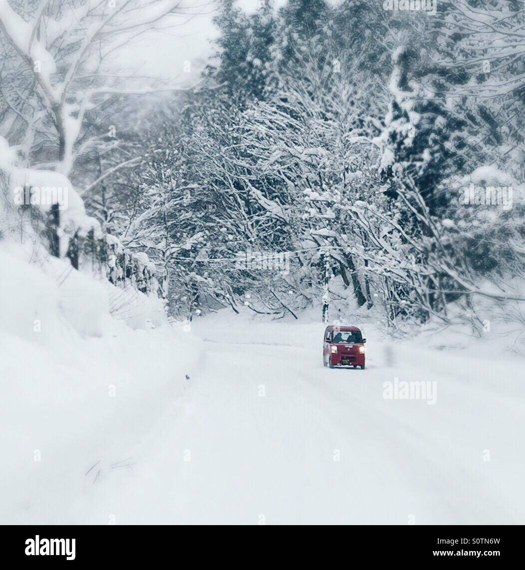 Coche rojo conducir sobre nieve las calles cubiertas de Shirakawago, Japón. Foto de stock