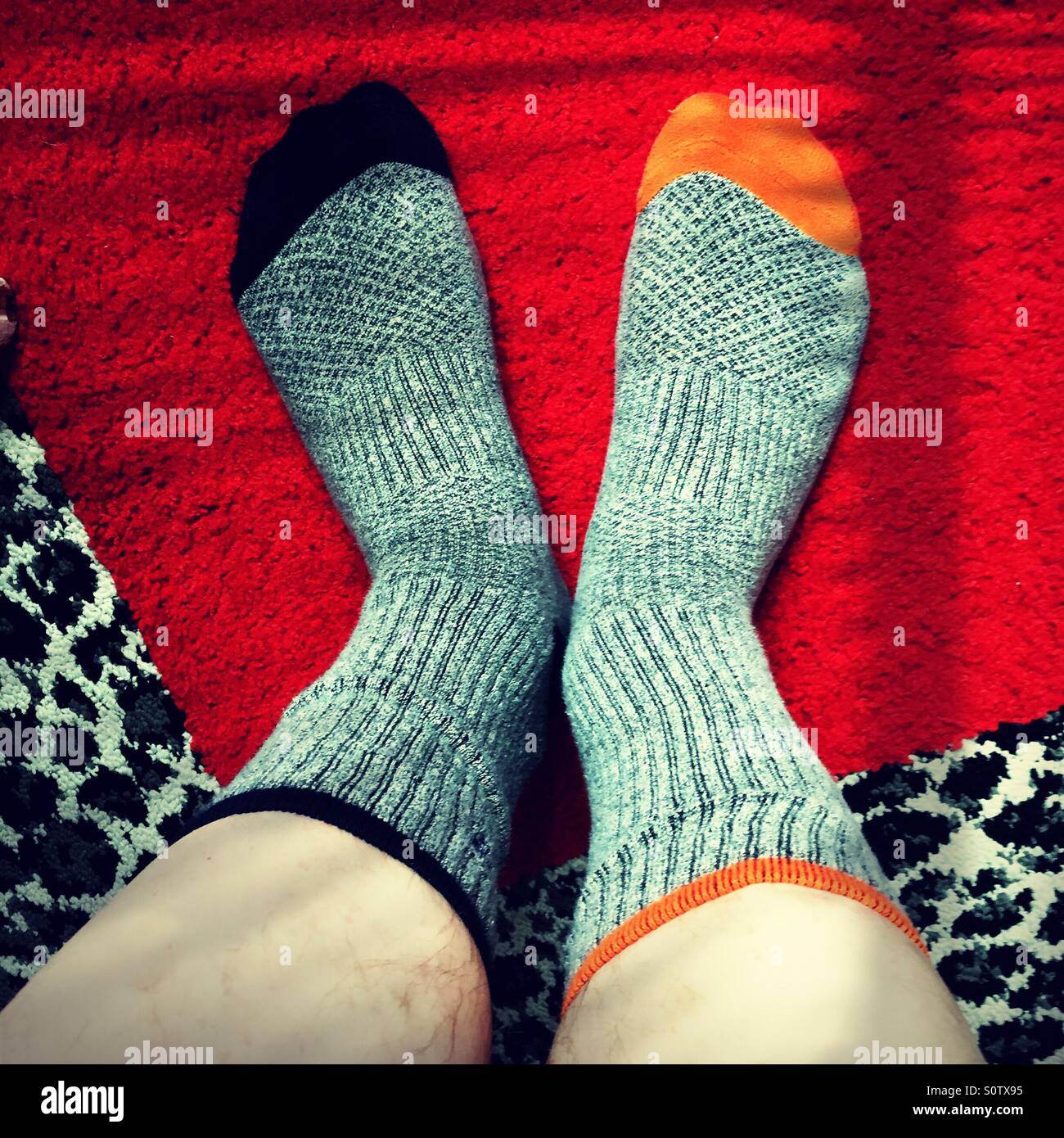 Hombre que llevaba calcetines gris no coincidentes con el azul y el naranja los dedos de los pies sobre una alfombra de leopardo y cuadrado rojo Foto de stock