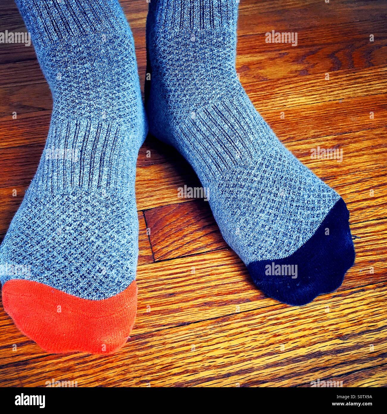 Hombre que llevaba calcetines gris no coincidentes con naranja y azul de los dedos de los pies sobre un piso de madera. Foto de stock