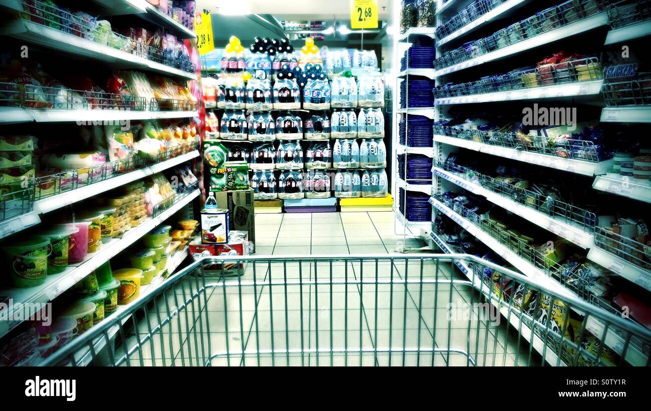 Empujar el carro de un supermercado haciendo su camino hacia abajo las estanterías de alimentos y abarrotes Foto de stock