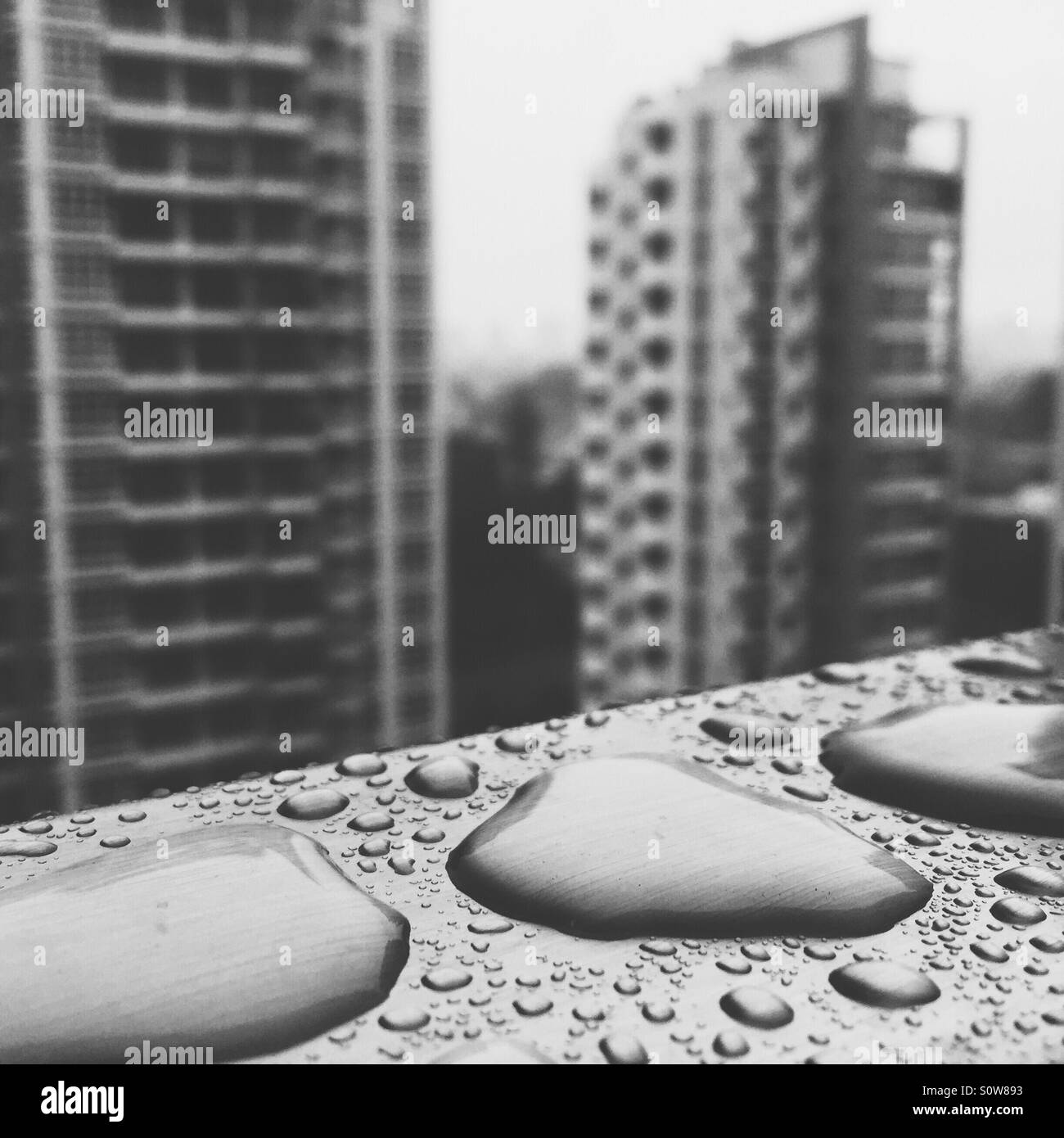 Las gotas de lluvia sobre una barandilla de acero inoxidable con un telón de fondo de edificios altos indican una estancia casa lunes Foto de stock