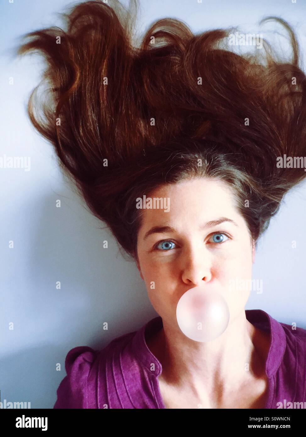 Mujer con cabello loco soplando un bubble gum bubble Foto de stock