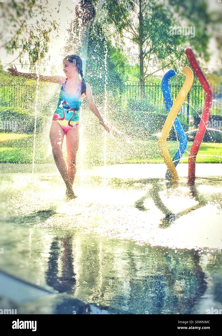 Chica en bañador jugando en la fuente de agua potable en verano Foto de stock