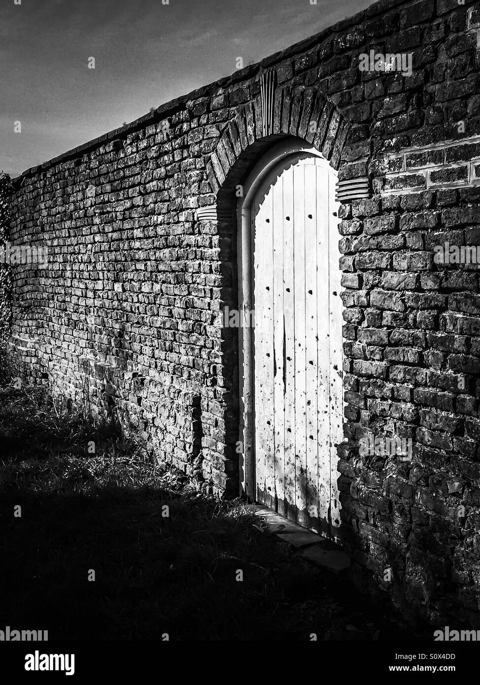 Puerta de madera arqueada en una vieja pared de ladrillos. Foto de stock