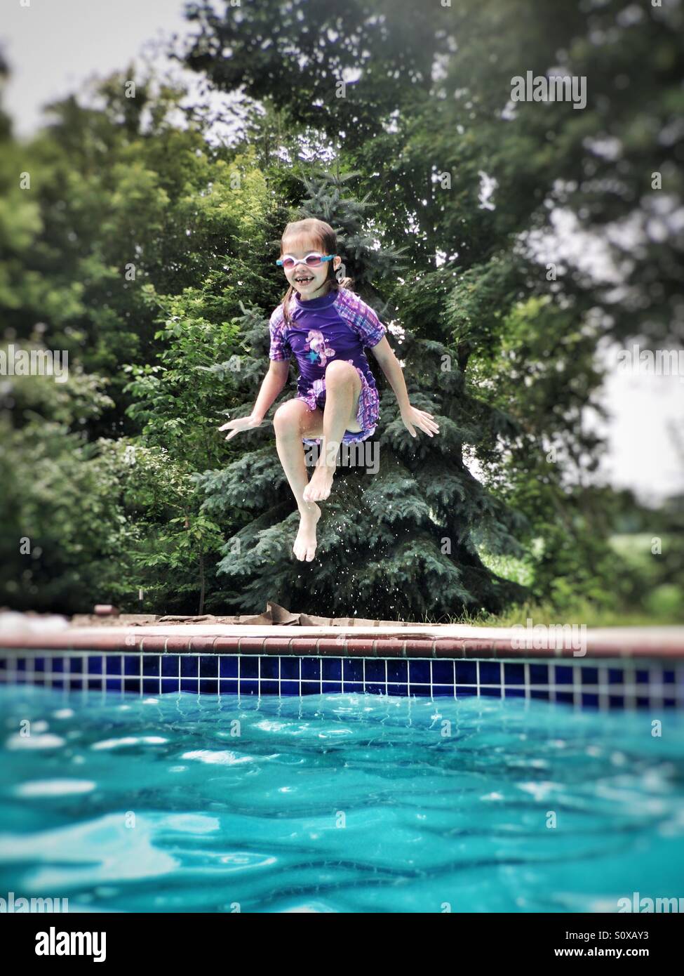 Vestida de traje morado y gafas de natación saltar en una piscina Foto de stock