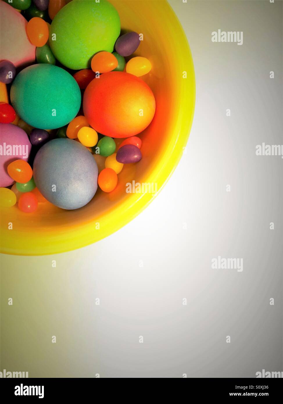 Huevos coloridos y jelly beans en un tazón visto desde arriba sobre fondo blanco. Foto de stock