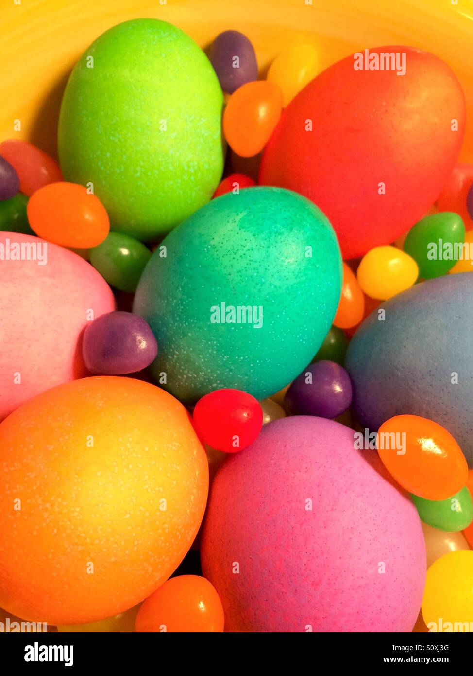 Huevos de colores brillantes y jelly beans en un recipiente amarillo, Vista cercana Foto de stock