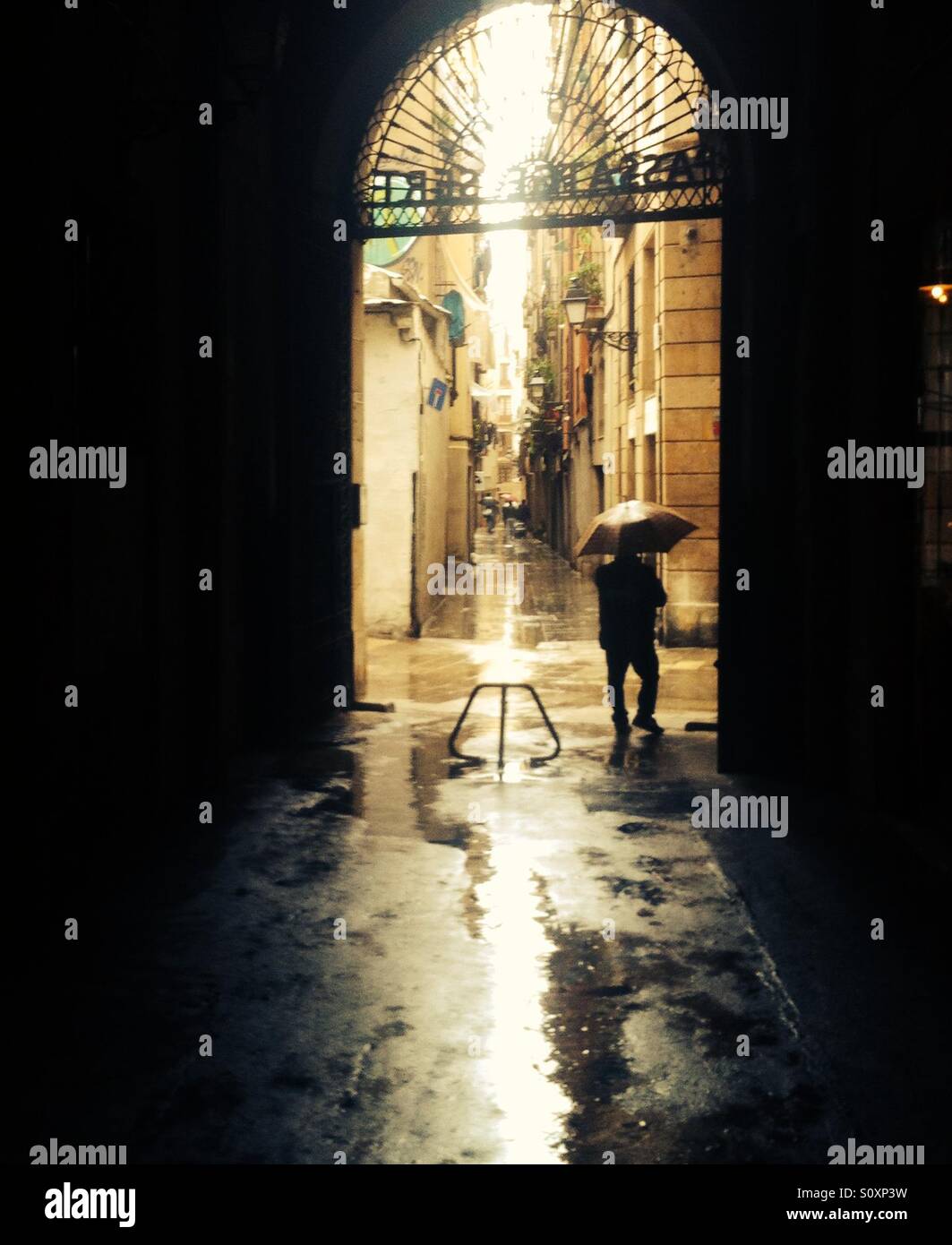 Un hombre camina bajo un paraguas por un pasaje de vieja de Barcelona Fotografía stock - Alamy
