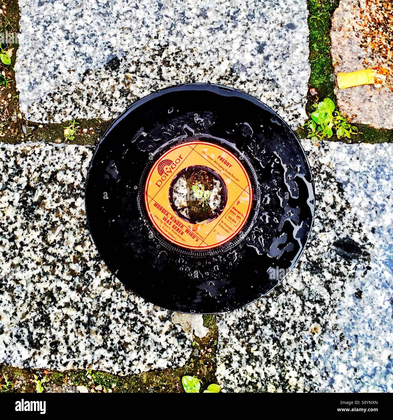 Disco de vinilo empapado por la lluvia en un suelo de piedra. Foto de stock