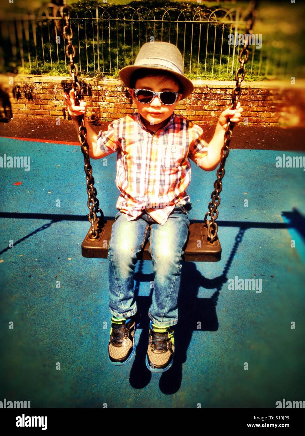 Un joven vistiendo gorra y gafas de sol juega el columpio en el parque. Foto de stock