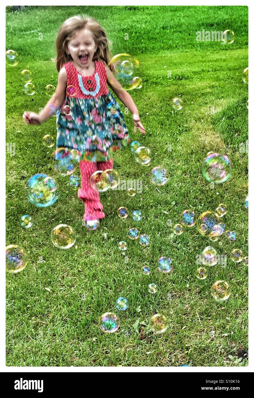Niña feliz corriendo a través de burbujas Foto de stock