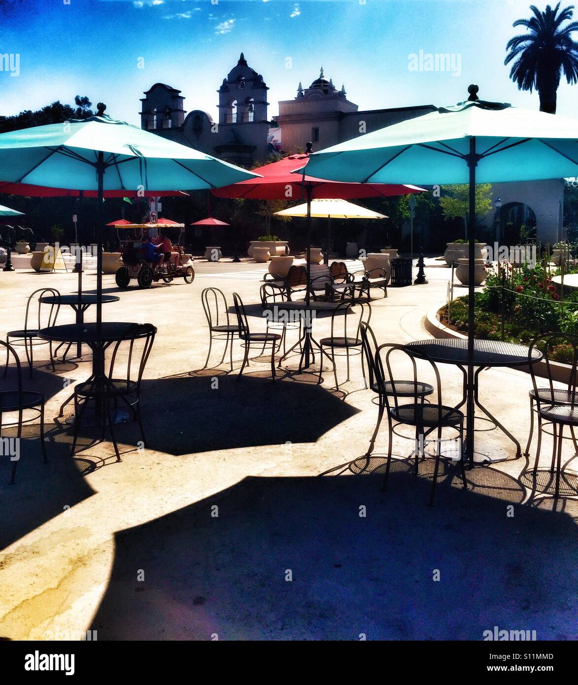 Zona para comer al aire libre en el parque Balboa en San Diego, CA. Zona de mesas y sillas negras de hierro, food court, área de comer en el exterior con luz brillante multicolor paraguas Foto de stock