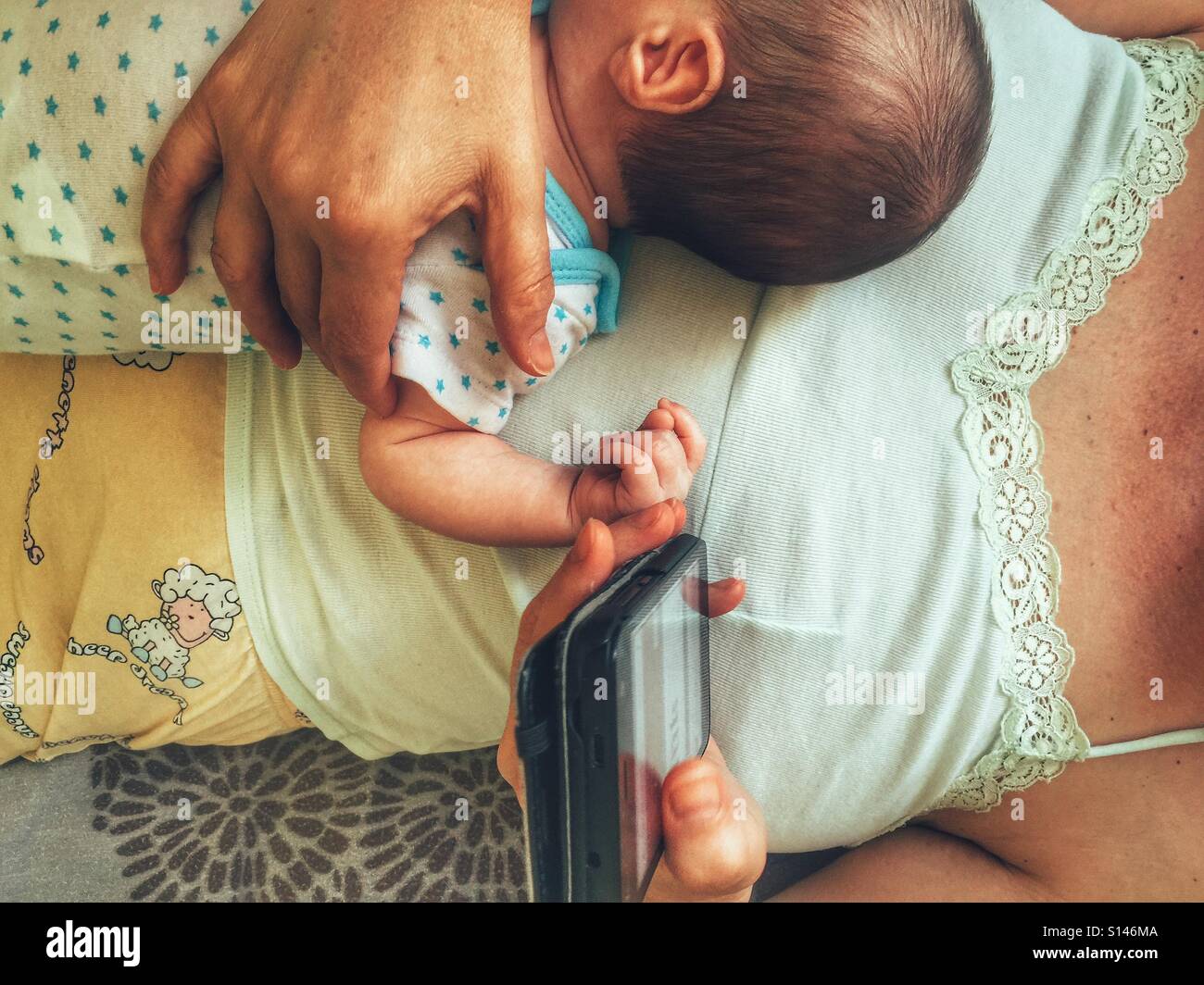 Madre mirando su smartphone y sostiene a su bebé Foto de stock
