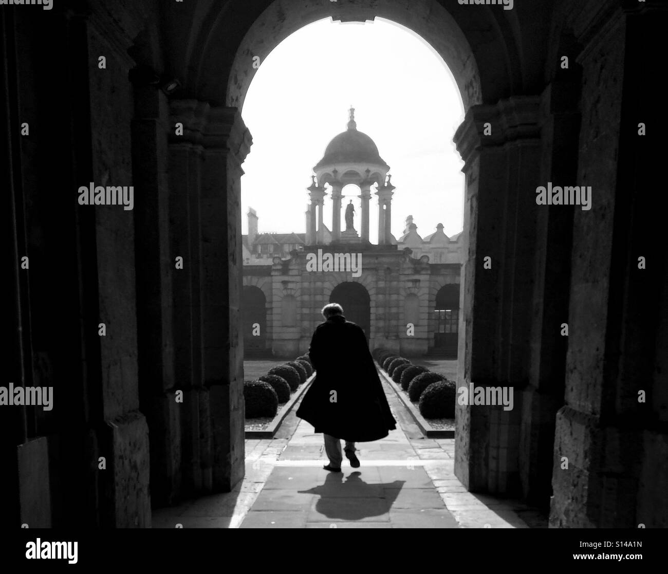 Becario en el Queen's College, Universidad de Oxford, camina a través de un arco de piedra que llevaba una bata académico tradicional. Foto de stock