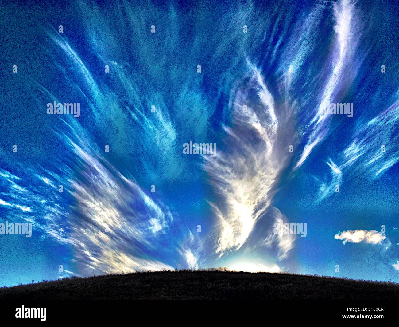 Feathery nubes contra el cielo azul sobre una colina baja Foto de stock