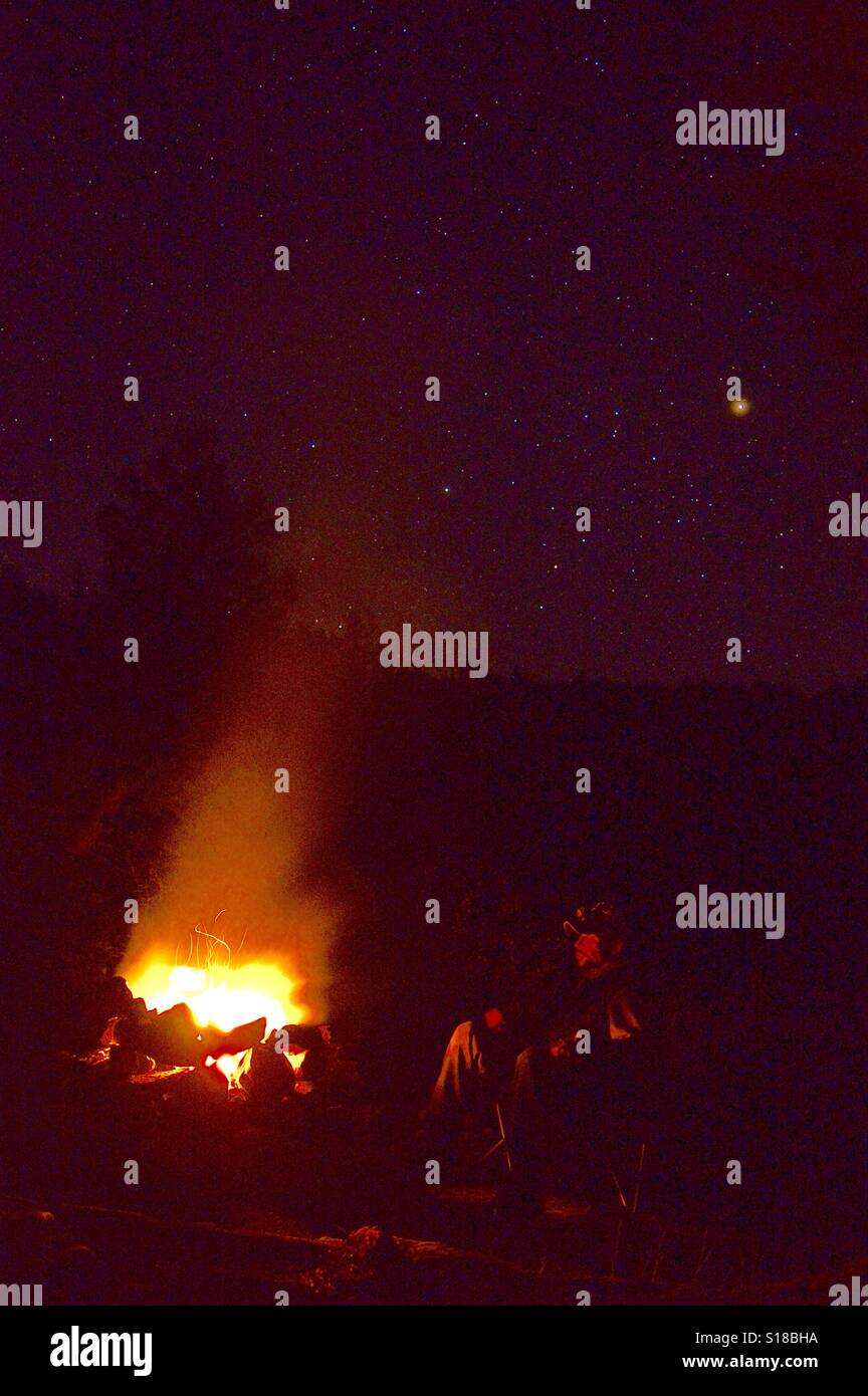 Persona en silla viendo noche fogata con el cielo lleno de estrellas retrato Foto de stock