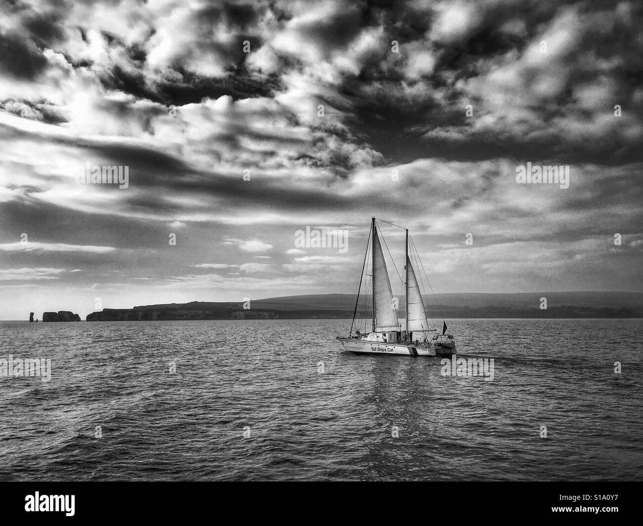 Fotografía en blanco y negro de un catamarán en el canal de la Mancha bajo un cielo espectacular frente a la costa de Dorset, Inglaterra, Reino Unido. Foto de stock