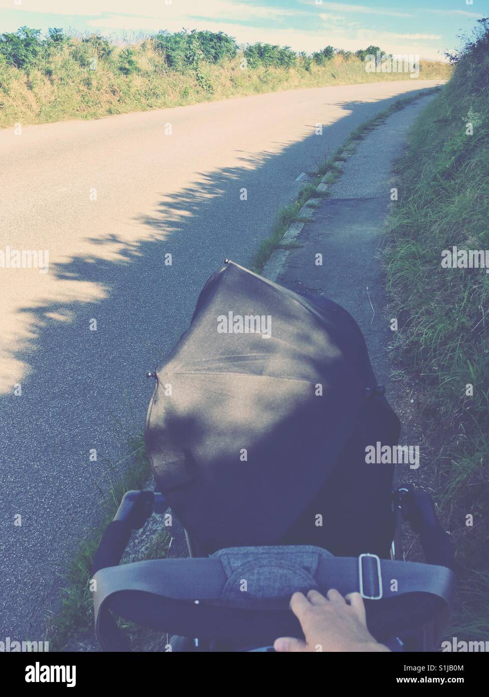 Perspectiva Personal caminando por un estrecho camino rural empujando un cochecito con una sombrilla en una preciosa y soleada mañana cálida en Cornualles, Reino Unido. Foto de stock