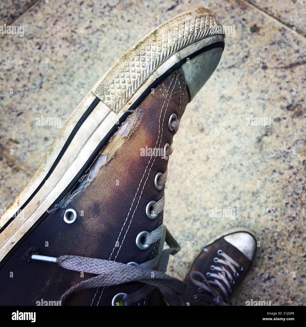 Un hombre el emplazamiento de cruzadas mostrando el agujero en su bien de zapatos Converse desgastados Fotografía stock - Alamy