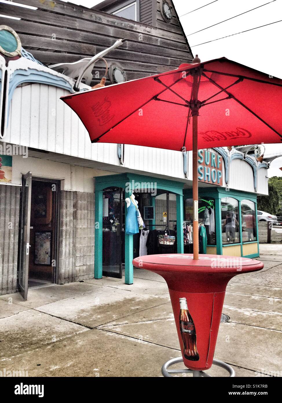 Tabla de color rojo y un paraguas en frente de una tienda de surf en Port Dover, Ontario. Foto de stock