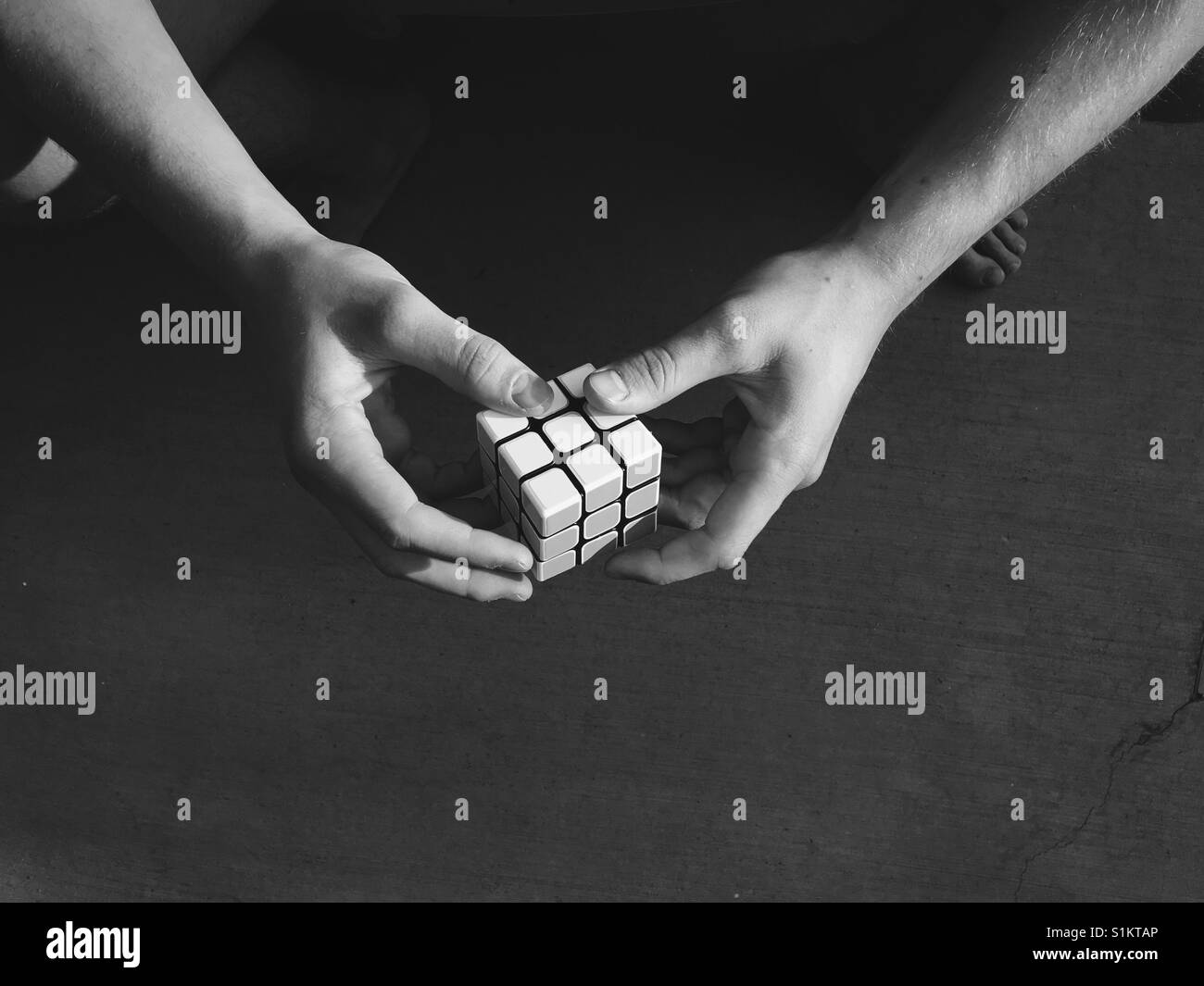 Primer plano de las manos de un hombre joven resolver un cubo rompecabezas. Cubo de velocidad. En blanco y negro. Foto de stock