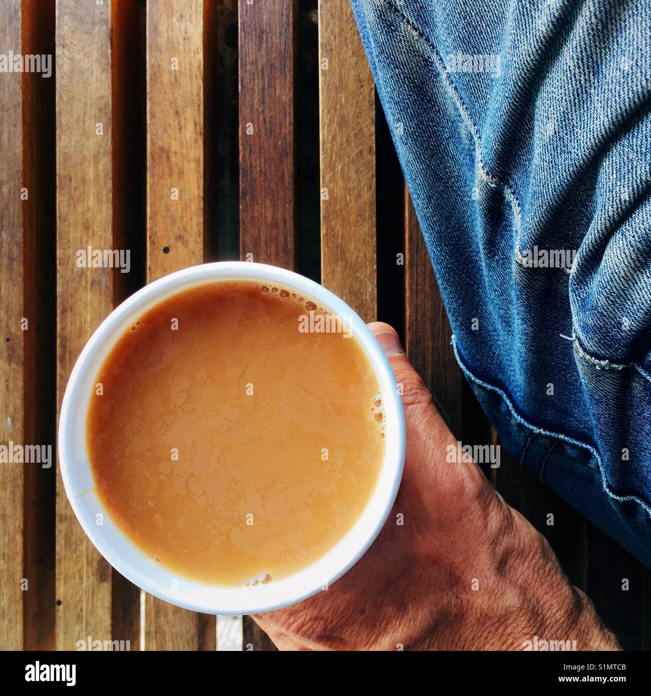 Una sobrecarga detalle shot de un hombre en jeans sosteniendo una taza de café recién hecho en una taza de papel Foto de stock