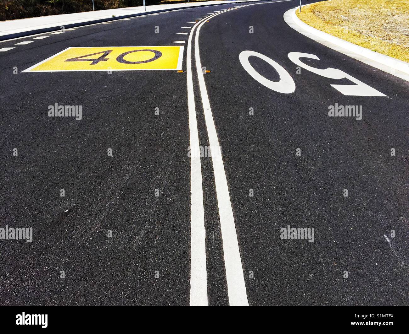 Doblar en carretera con líneas dobles, grandes del límite de velocidad de 50 y 60 pintados sobre el asfalto. Australia Foto de stock