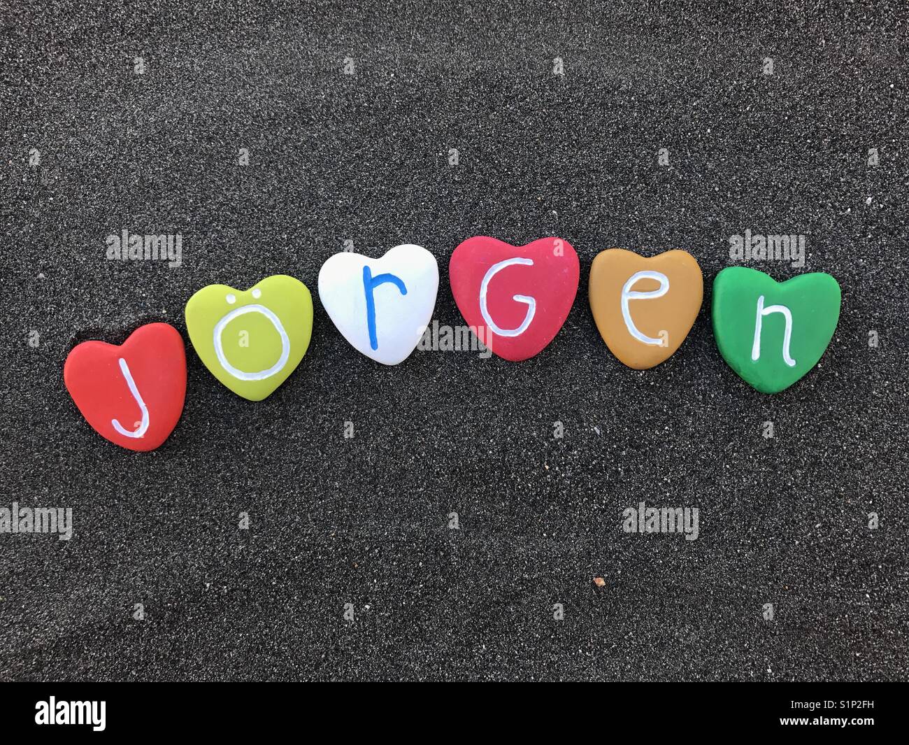 Jörgen, nombre masculino con piedras de color sobre arena volcánica negra Foto de stock