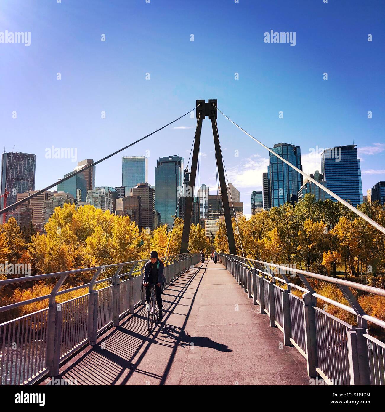 Un ciclista pedales lejos del centro de la ciudad de Calgary, Alberta, Canadá por un puente sobre el río Bow en un hermoso día de otoño Foto de stock