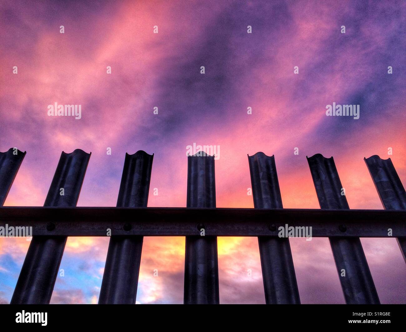 Una valla metálica dura representando confinamiento bajo un colorido atardecer cielo Foto de stock