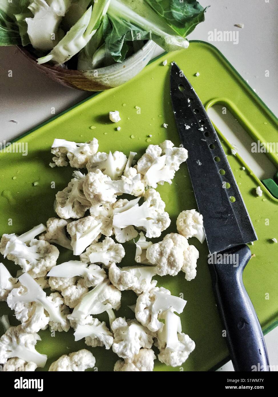 La coliflor picada en verde brillante junto a la placa de corte de cuchilla del chef. Foto de stock