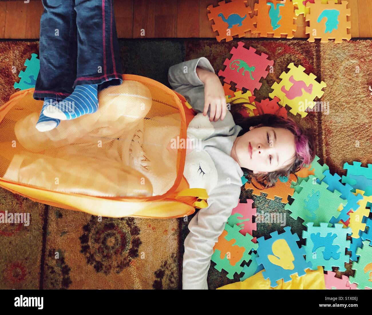 Chica sentar en el suelo con las piezas del rompecabezas de espuma en una  malla naranja toy bin y otra niña descansando en sus pies Fotografía de  stock - Alamy