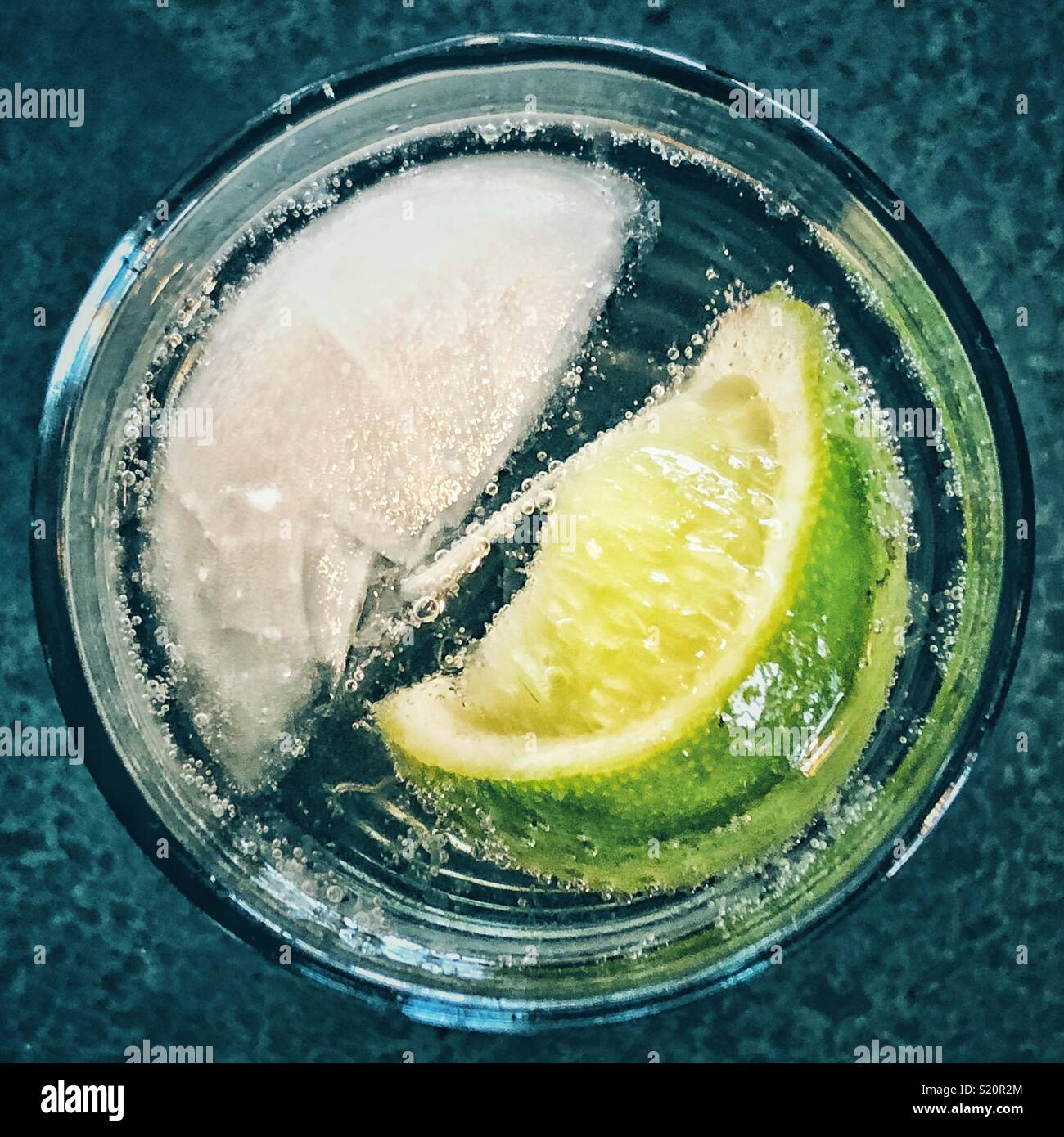 Vista superior de un solo cubo de hielo y gajo de lima en un vaso de agua con gas Foto de stock