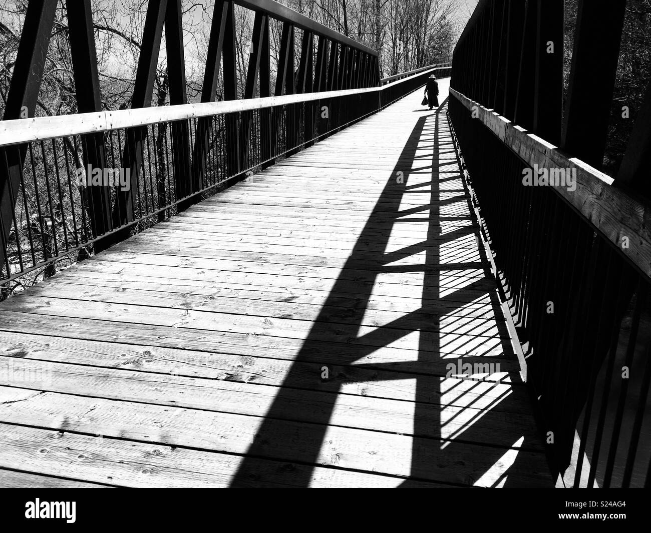 Persona solitaria caminando sobre un puente de madera. Blanco y negro. Foto de stock