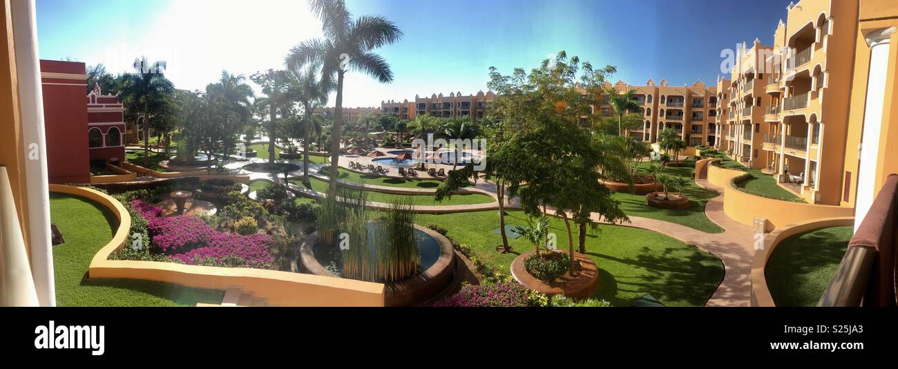 Vista panorámica con sun flare palmeras y piscina, hotel encantador que rodea el verdor en medio Foto de stock