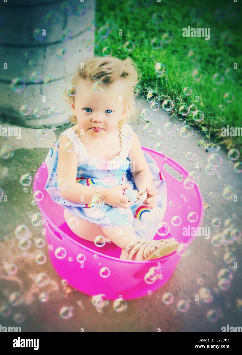 Bebé sentado en una cuchara rosa rodeado de burbujas Foto de stock