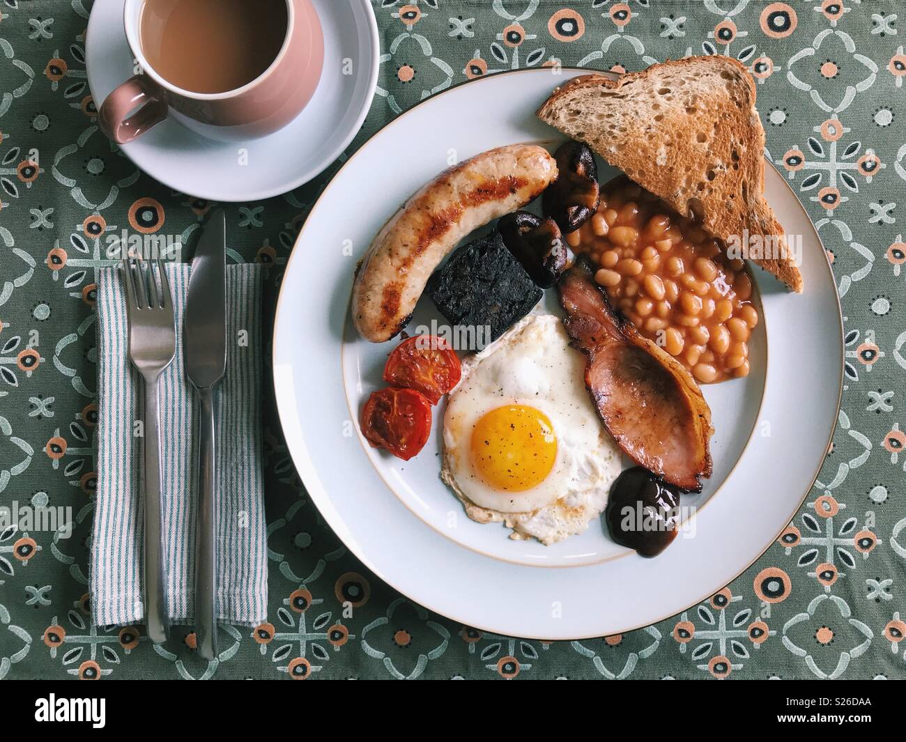 Vista aérea de un desayuno inglés completo casera, con salchichas, tomates, morcilla, setas, alubias, tostadas, salsa marrón, un huevo frito, y una taza de té. Foto de stock