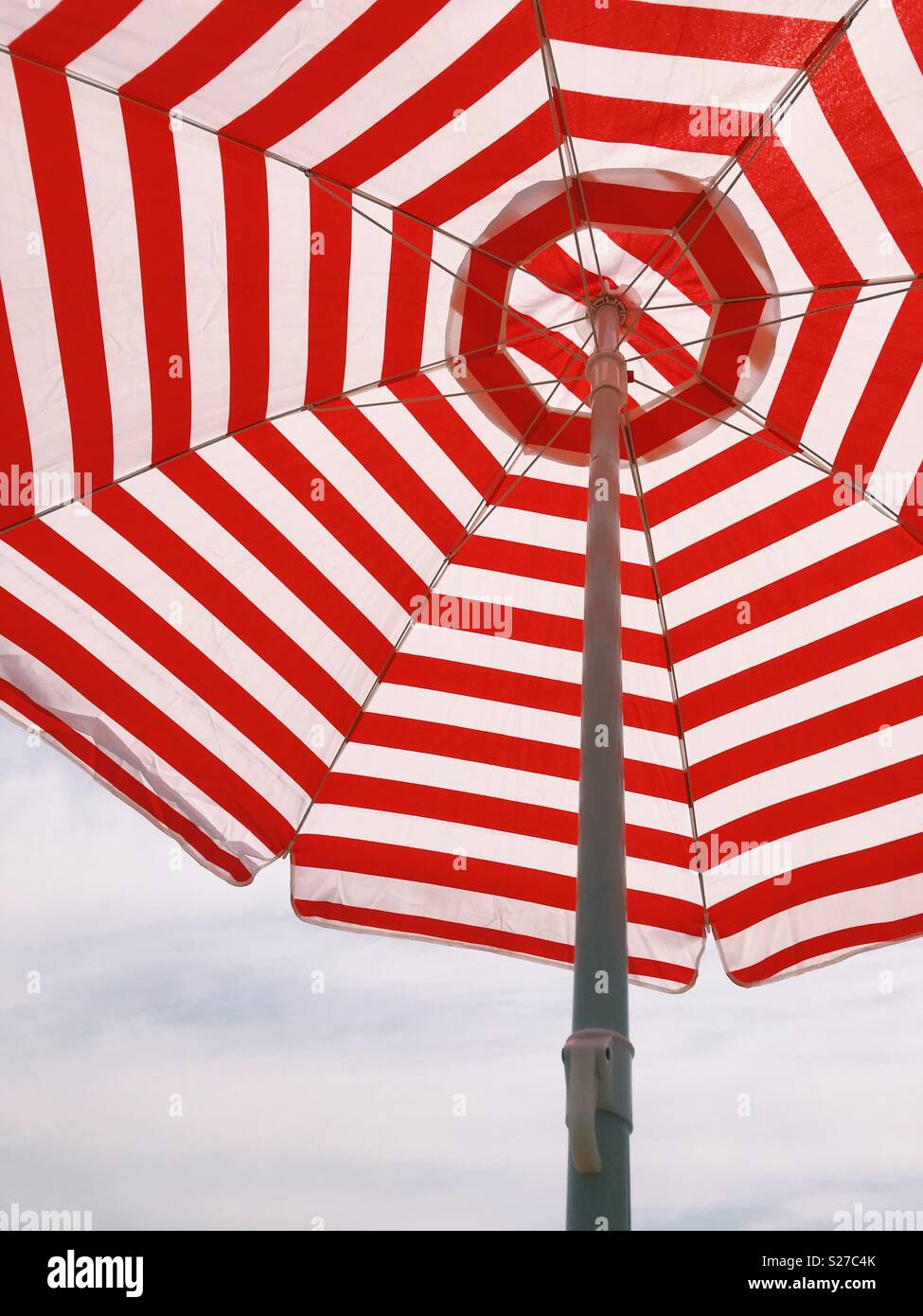 Mirando hacia arriba a rayas rojas y blancas de una sombrilla en la playa. Foto de stock