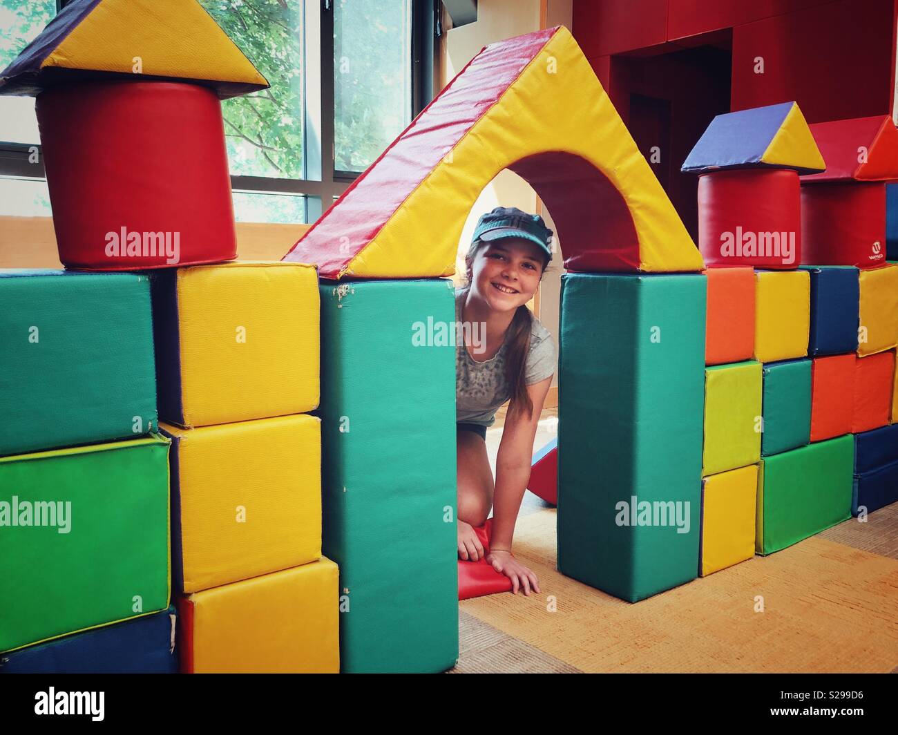 11 años de edad, niña peeking a través de la puerta del castillo de bloque grande en una zona de juegos interior Foto de stock