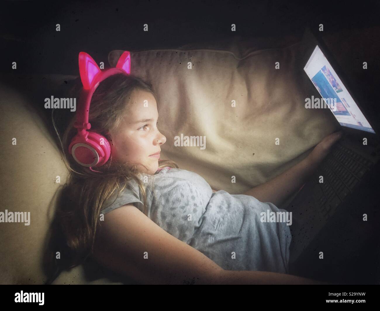 11 años de edad, vestida de luz neon pink auriculares viendo videos en un portátil. Foto de stock