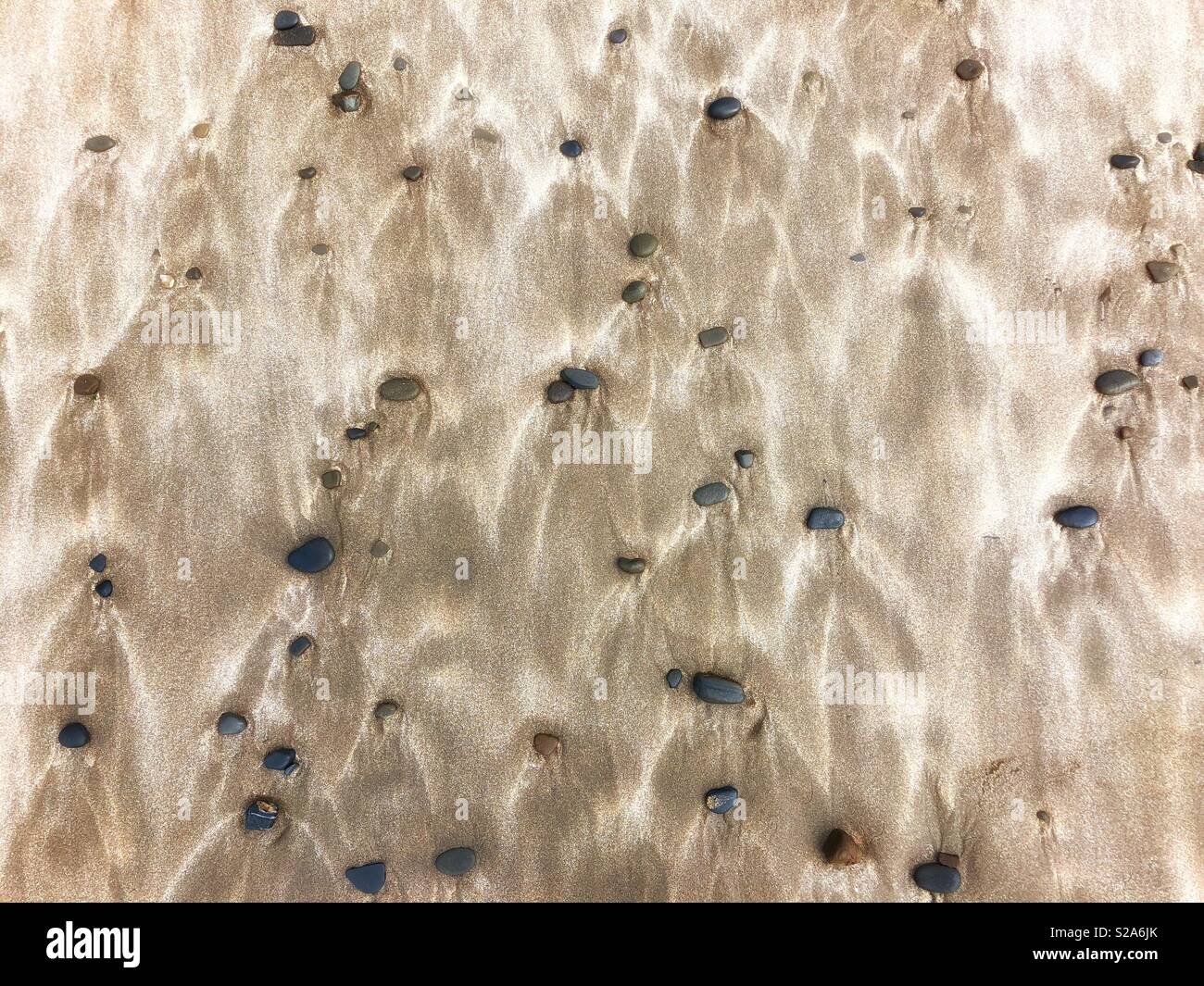 Los guijarros y la arena soplada por el viento patrones en una playa Galés. Foto de stock