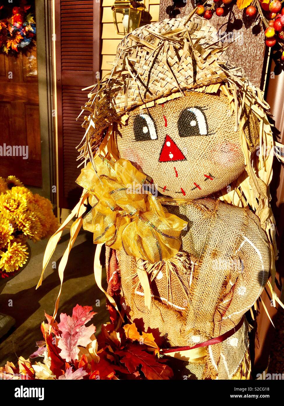 Lindo espantapájaros con oro bow hat y sacos de arpillera otoño colorido rodeado de flores y hojas y bellotas Foto de stock