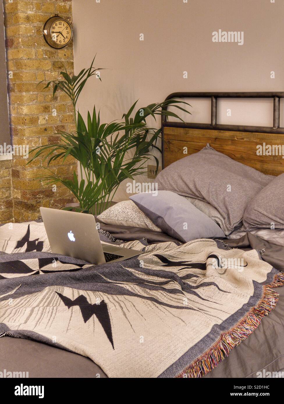 Cama desordenada en estilo loft dormitorio chic industrial con palmera y mac portátil Foto de stock