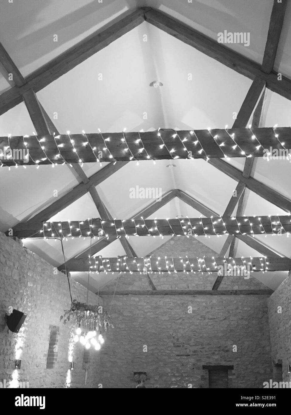 Un techo abovedado en una casa de granja británica con las luces de hadas a través de las vigas de madera en monocromo. Foto de stock