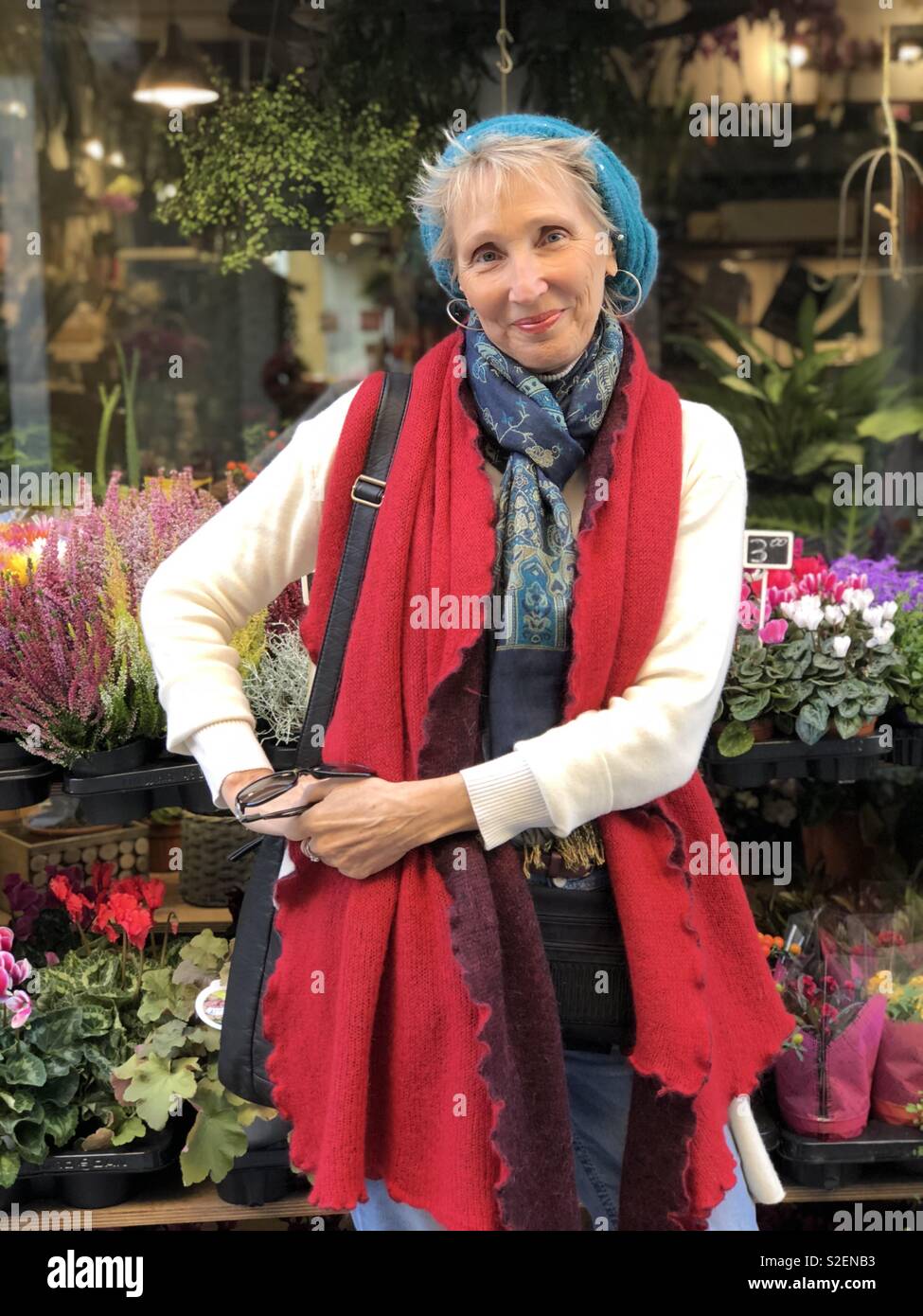 Mujer de 59 años con mantón rojo y sombrero azul de pie delante de la tienda de flores en Venecia Italia Foto de stock