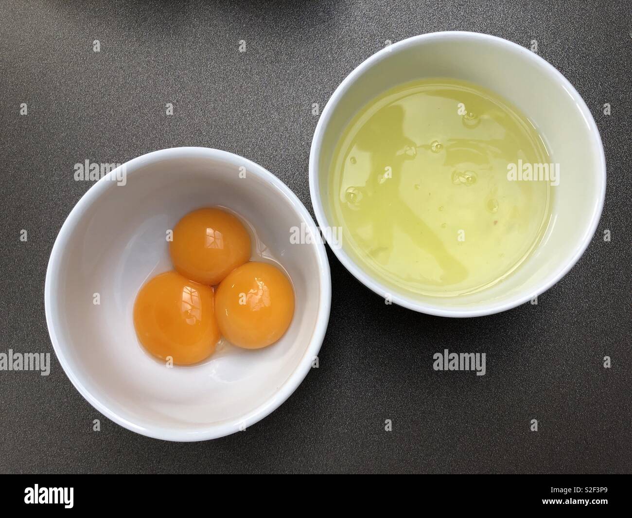 3 huevos separados en yemas y claras contenidas en 2 cuencos blancos lisos Foto de stock