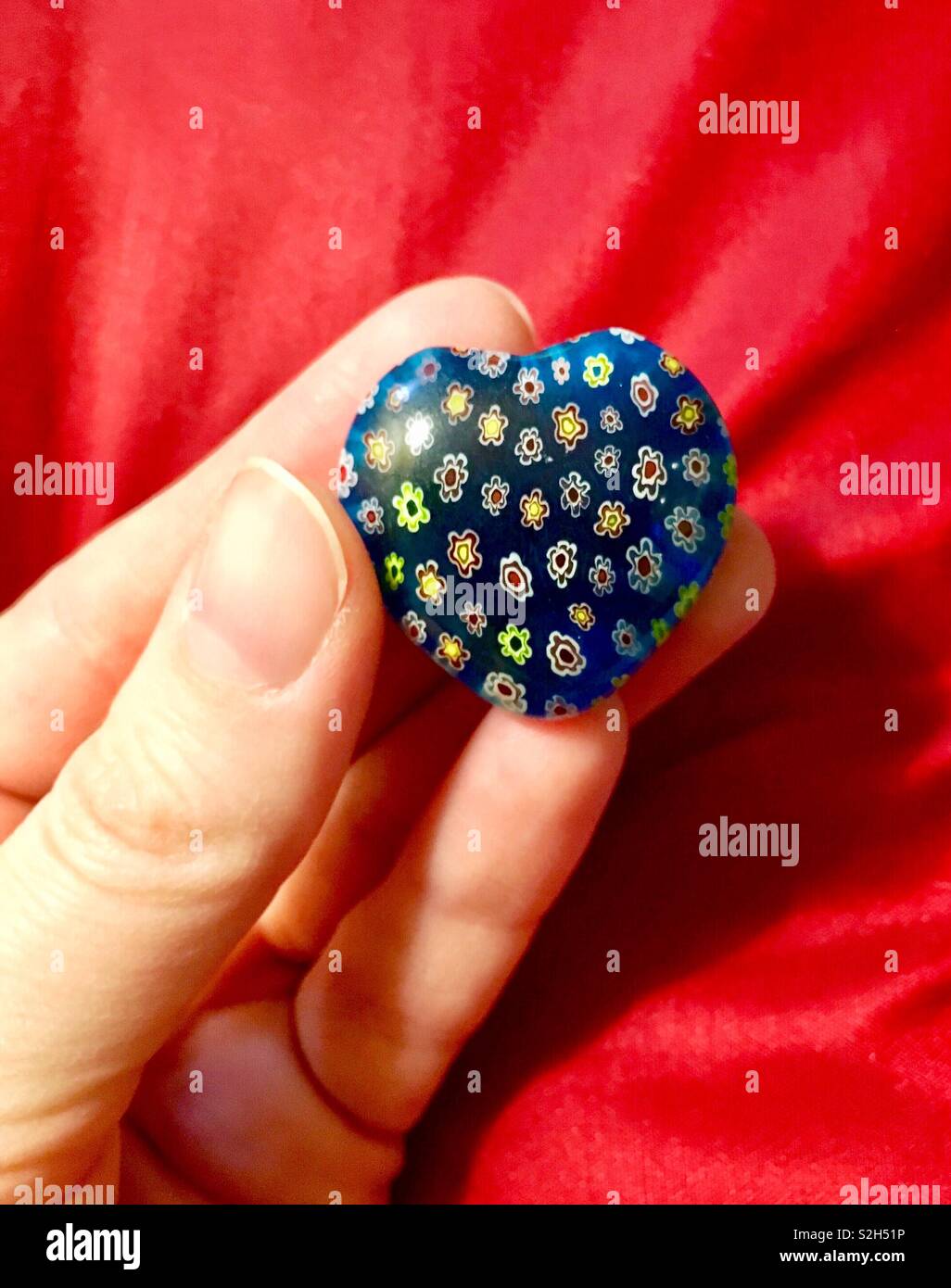 Mujer sosteniendo el corazón de cristal azul con pequeñas flores de colores contra un fondo rojo para el Día de San Valentín Foto de stock